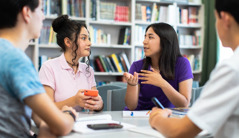 Tjejen från förra bilden pratar med sina klasskompisar i biblioteket på skolan.