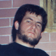 Artan Brahja da giovane con barba e capelli lunghi.