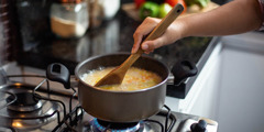 Жінка помішує суп, який вариться на газовій плиті.