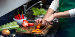 A woman chopping fresh vegetables on a wooden cutting board.