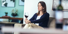 Uma mulher olha para o seu copo de vinho enquanto está sentada sozinha em casa.