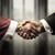 高価な金のアクセサリーを身に着けた聖職者とビジネスマンが握手している。