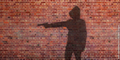 拳銃を持った人の影がれんがの壁に映し出されている。