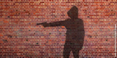 A shadow on a brick wall of a person pointing a gun.