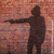 A shadow on a brick wall of a person pointing a gun.