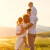 Tata drži jedno dete na ramenima, mama drugo u rukama, i svi posmatraju sunce na horizontu