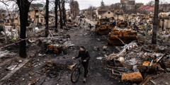 A man pushing his bike along a war-ravaged street littered with debris and destroyed military vehicles.