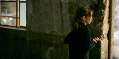 Una niña en un edificio en ruinas mira hacia afuera desde una abertura en la pared.