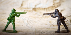 Два игрушечных солдатика стоят на карте, нацелив друг на друга ружья.