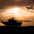 Silhouettes d’un tank et d’un drone de combat devant un coucher de soleil.
