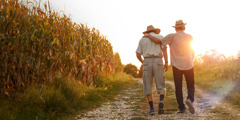 Two elderly men walking together down a path at sunset. One has his arm on the shoulder of the other.