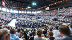 Convention attendees watching a video in a large arena.