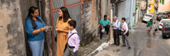 Pairs of Jehovah’s Witnesses preaching on a narrow street in a São Paulo suburb, using the brochure “Enjoy Life Forever.”