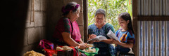 En una casa, una testigo de Jehová y su hija le leen un texto bíblico a una señora que está preparando la comida.