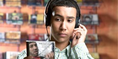 A teenage boy wearing headphones and listening to music as he examines a CD cover.