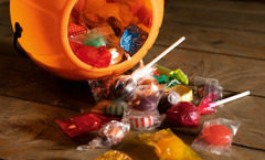 An orange pumpkin-shaped bucket laying on its side and spilling assorted candy onto a table.