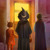Három gyerek halloweeni jelmezben áll egy ház ajtaja előtt, amely fel van díszítve halloweeni dekorációval.
