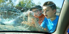 Två unga killar tittar på framrutan på en bil som de har krossat med en boll