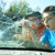 Two young boys looking at a car’s windshield broken by their baseball