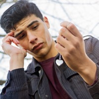 An emotionally distraught young man holds a heart-shaped necklace