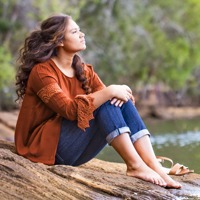 A teenage girl sits beside a lake