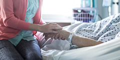 A young woman holds an older person’s hand in a hospital