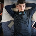 A teenage boy has many electronic devices, but he lays on his bed and stares at the ceiling