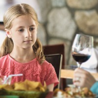 A little girl observes her mother drink wine