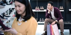 A husband waits impatiently while his wife shops for shoes