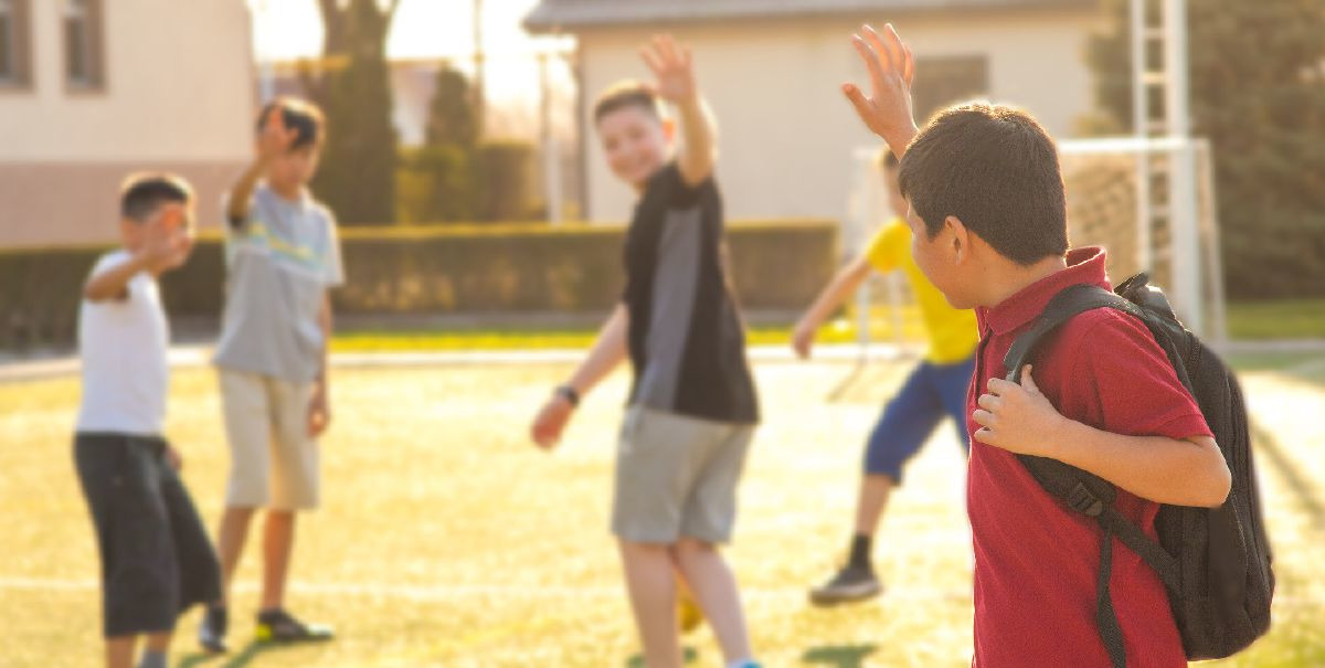 Un garçon fait au revoir de la main à ses copains d’école