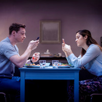 A husband and wife each use a smartphone while they are eating a meal.