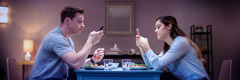 A husband and wife each use a smartphone while they are eating a meal.