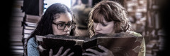 Two teenage girls look at an old book that features the occult