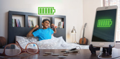 A teenage boy wakes up after getting adequate sleep; a cell phone is charging near his bed