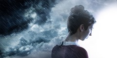 En kvinne står under mørke skyer i regnvær og tenker negativt