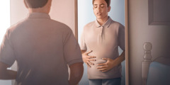 A teenage boy looks at his stomach in a mirror