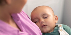 A mother gazing at her sleeping baby in her arms.