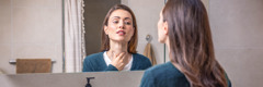 Frente a un espejo, una mujer se toca el cuello para comprobar si tiene algún problema en la tiroides.