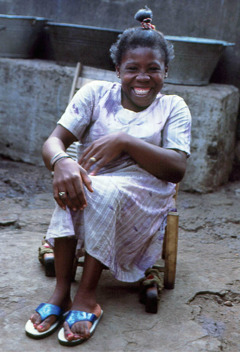 A young Jay smiling as she sits on a small cart with wheels.
