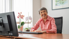 Irma sorrindo em seu escritório, sentada em frente a um computador.