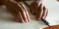 Una mujer ciega lee con sus dedos una publicación en braille.