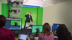 Ein Übersetzerteam bei der Aufnahme einer Publikation in Gebärdensprache. Der Sprecher steht vor einem grünen Hintergrund.