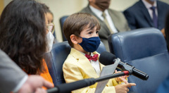 A young boy commenting at a congregation meeting while a boom microphone is held in front of him. He and the other attendees are wearing masks.