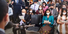 A sister commenting at a congregation meeting. A brother holds a boom microphone for her. All in the audience are wearing masks.