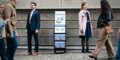 Um casal sorrindo ao lado de um carrinho de publicações que está com o cartaz do curso bíblico.